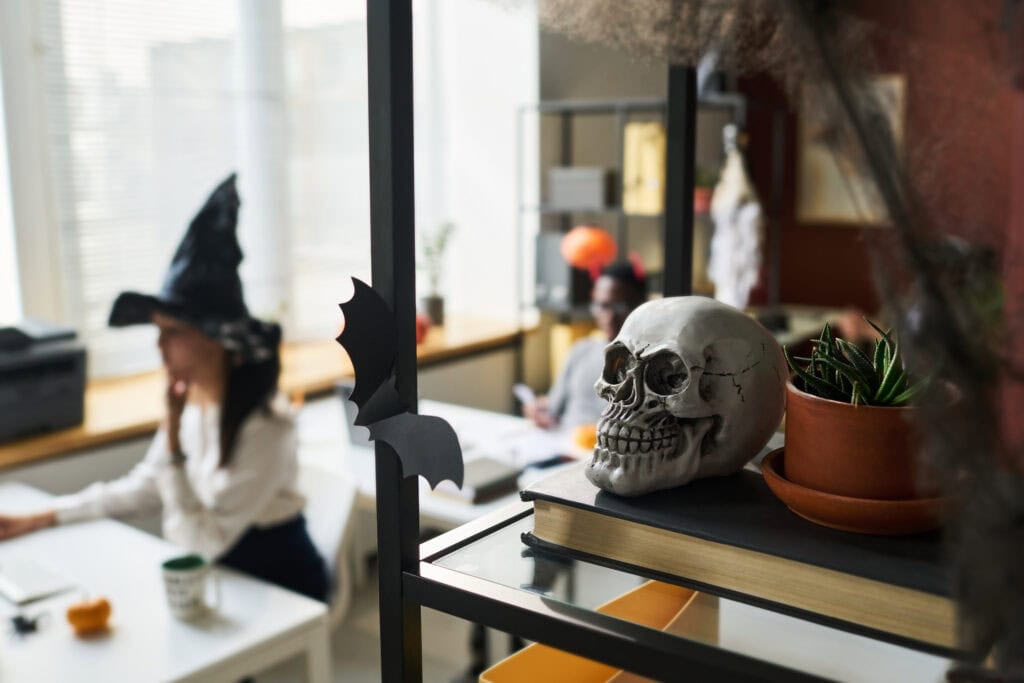 A decorated office desk with Halloween-themed decorations including mini pumpkins, cobwebs, and spooky figurines.