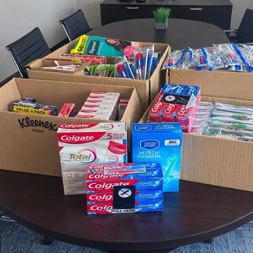 Boxes filled with donated hygiene products, including toothpaste, toothbrushes, flossers, tissues, and other essentials.