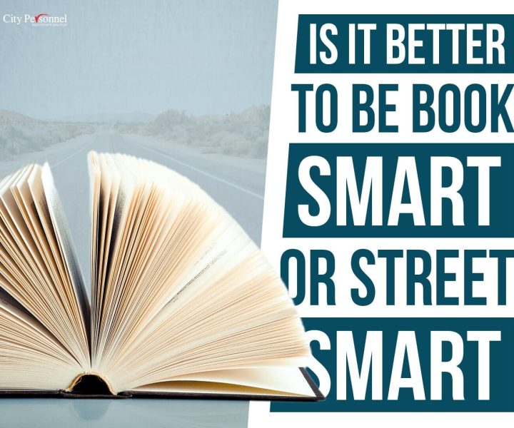 A promotional graphic from City Personnel featuring an open book with fanned-out pages in the foreground. The background shows a blurred desert road stretching into the distance. Bold text on the right side reads, "IS IT BETTER TO BE BOOK SMART OR STREET SMART?" in a mix of uppercase and bolded words. The City Personnel logo is positioned in the top left corner. The image visually contrasts academic knowledge (book) with real-world experience (road).